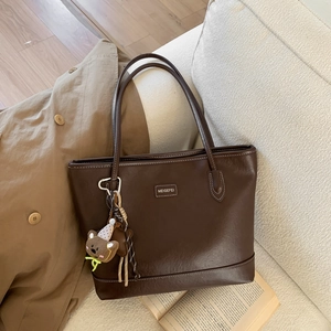 Detail of dark brown faux leather tote with plush bear charm on a minimalist sofa