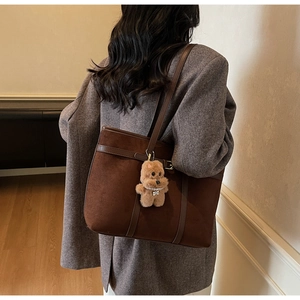 Detail of dark brown suede tote bag with plush bear charm and leather shoulder strap