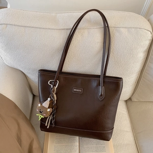 Close-up of vintage brown tote bag with white stitching and cute plush bear charm decoration