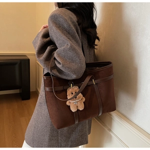 Detail of a large brown suede tote bag with a plush bear charm on a model's shoulder