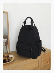 Close-up of minimalist black backpack with handle, shown in a clean home interior setting