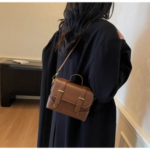 Detail of a brown leather vintage satchel bag worn by a model in a black winter coat