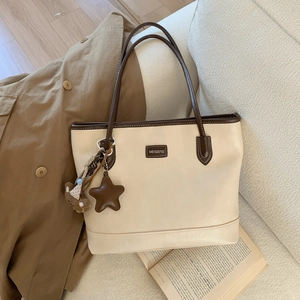 Detail of cream and brown contrast tote bag with star and bear charms on a sofa