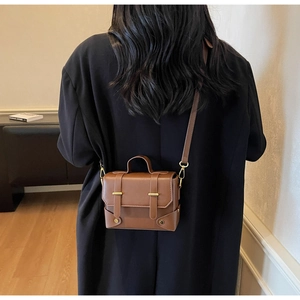 Rear view of model carrying brown square crossbody bag with gold hardware and top handle
