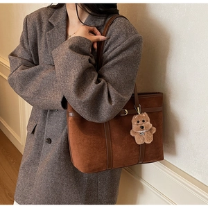Detail of a brown suede tote bag with leather straps and a cute plush doll pendant