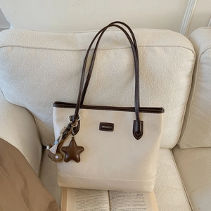 Detail of cream leather tote bag featuring brown trim and a cute teddy bear charm
