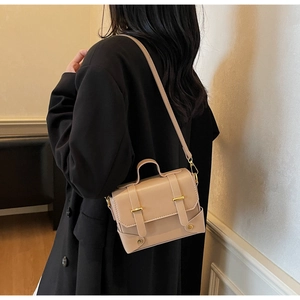 Side view of beige matte leather messenger bag worn over a black coat in a minimalist setting