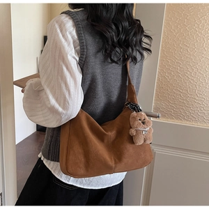 Brown suede hobo bag shown on shoulder featuring a cute plush bear charm with pearls