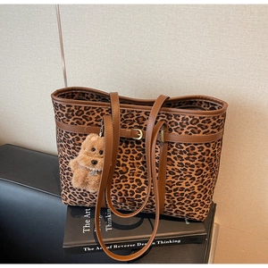 Detail of leopard print tote bag with brown leather straps and cute dog plush charm