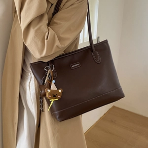 Detail of dark brown leather tote bag with contrast stitching and bear charm