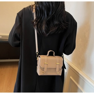 Light brown crossbody square bag with leather straps on a black blazer backdrop