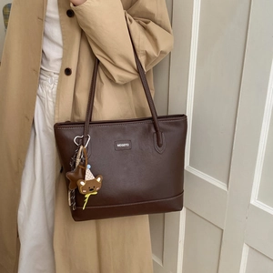 Close-up of a vintage dark brown tote bag with a bear charm on a model in a trench coat