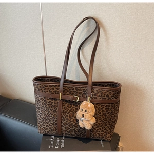 Detail view of leopard print tote bag with brown leather straps and plush puppy charm