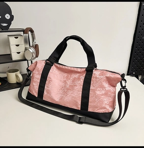 Pink travel bag with black straps and adjustable shoulder strap on a desk setting