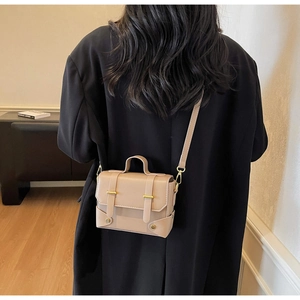 Detail of a beige vintage square crossbody bag with gold buckles and leather handle