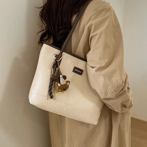 Detailed side view of a cream tote bag with brown trim and cute plush bear charm accessory