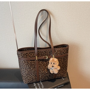 Leopard print tote bag with brown leather handles and plush dog charm on a book