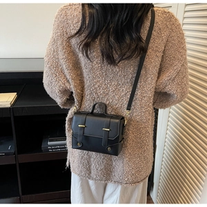 Detail of a black matte leather square bag with gold buckle shown on a female model