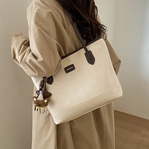 Detail of a cream tote bag with brown leather handles and a cute bear charm on a model