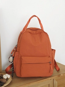 Orange nylon outdoor backpack with large capacity and owl charm on a wooden shelf