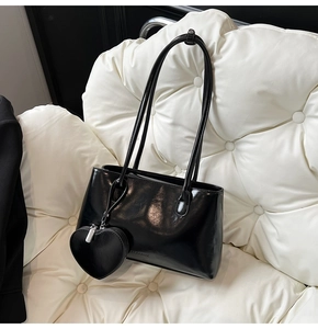 Detail of black oil wax leather tote with heart charm and subtle embossed logo on base