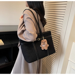 Detail view of large black suede tote bag with leather straps and plush bear charm