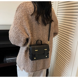 Detailed view of a black leather square bag with gold metal buckle and rivets on crossbody