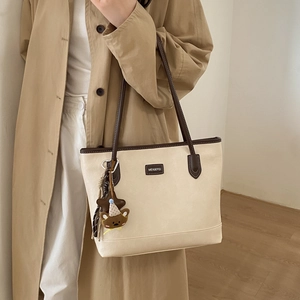 Detail of a large beige tote bag with brown straps and cute teddy bear bag charm