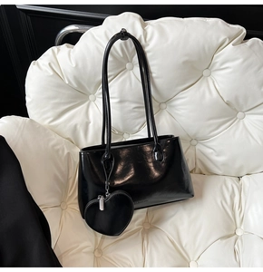 Detail of black glossy tote bag with heart charm and brand logo on white quilted chair