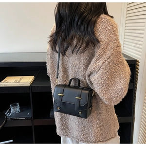 Detail shot of black matte leather square bag with gold hardware and flap closure details