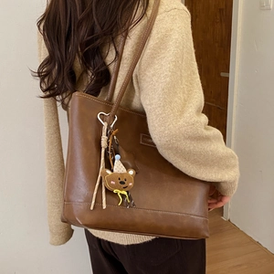 Detailed view of a vintage brown tote bag with white stitching and bear plush charm