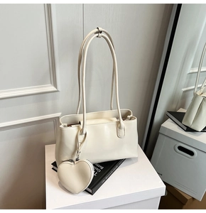 Close-up of cream oil wax leather tote bag with heart-shaped charm on white pedestal