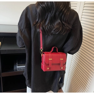 Detail of red square crossbody bag with gold hardware shown on a black shirt