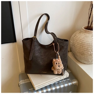 Détail d'un sac cabas marron avec charm en peluche sur une valise argentée
