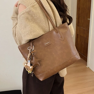 Brown faux leather tote bag detail with decorative teddy bear and star bag charms