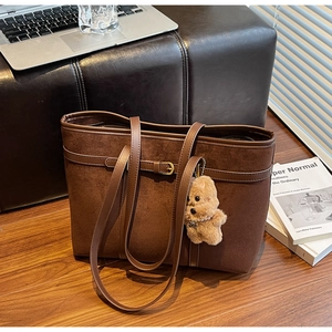 Detail of a large brown suede tote bag with a plush puppy charm on a wooden floor