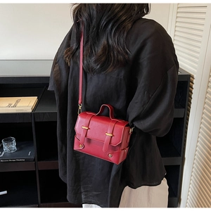 Detail shot of a dark red crossbody bag with golden metal buckles and matte leather texture