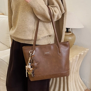 Detail of a dark brown vintage tote bag with white stitching and a cute bear charm