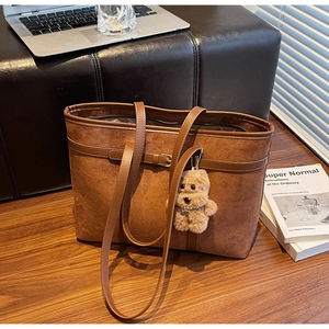 Detail of a brown suede tote bag featuring a cute teddy bear charm in a cozy home setting