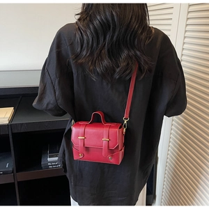 Model wearing a red structured square handbag with a gold clasp and crossbody strap