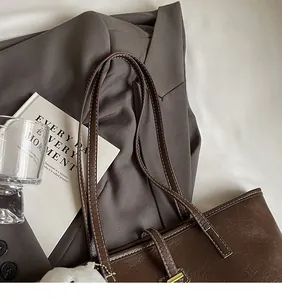 Detail of a brown leather tote bag showing fine stitching and slim long shoulder straps