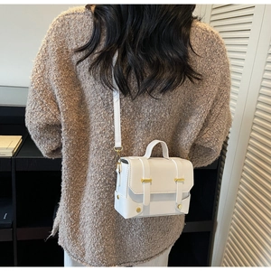 Detail shot of minimalist white leather square bag with gold bar and metal hooks