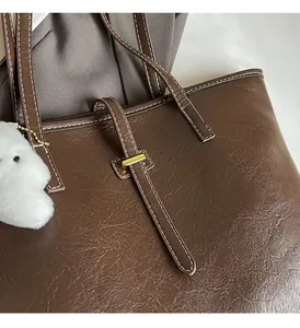 Detail of brown tote bag with contrast stitching, gold metal buckles and puppy charm