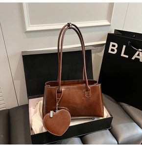 Deep brown oil-wax leather shoulder bag with heart charm inside a black gift box