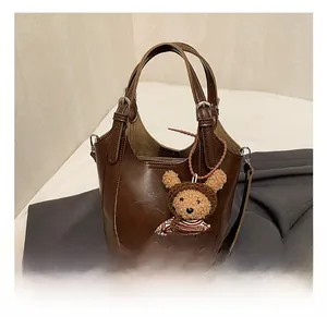 Detail of dark brown leather bucket bag with a cute plush bear charm on a minimal background