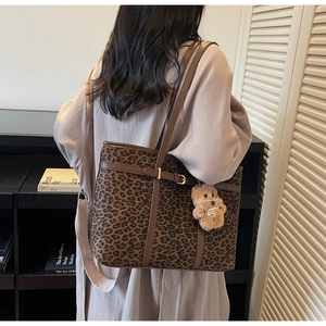Detail of leopard print tote bag with brown leather straps and plush bear charm