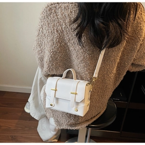 Close-up of a white structured crossbody bag with gold hardware on a knit sweater