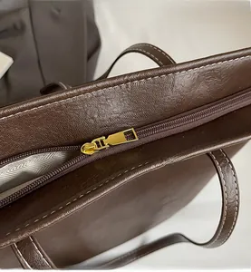 Detail of dark brown leather tote featuring white stitching and gold metal zipper