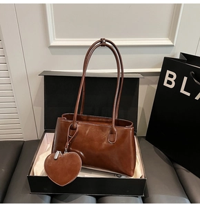 Detail of dark brown oil wax leather tote bag featuring a heart-shaped charm in a gift box