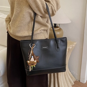 Detail of black PU leather tote bag with white stitching and cute bear charm
